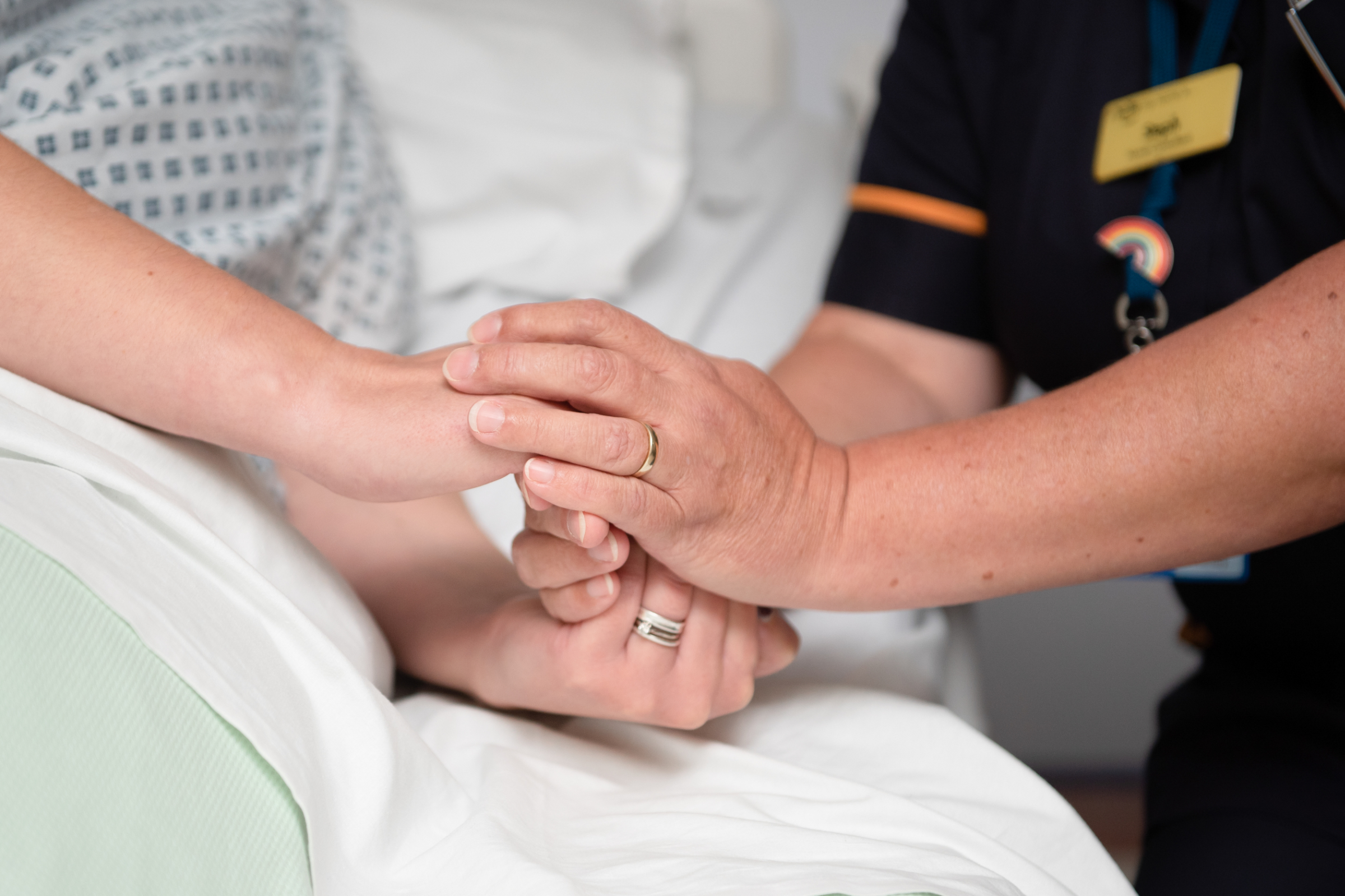 Close up of a healthcare worker holding the hand of a patient in a hospital bed.