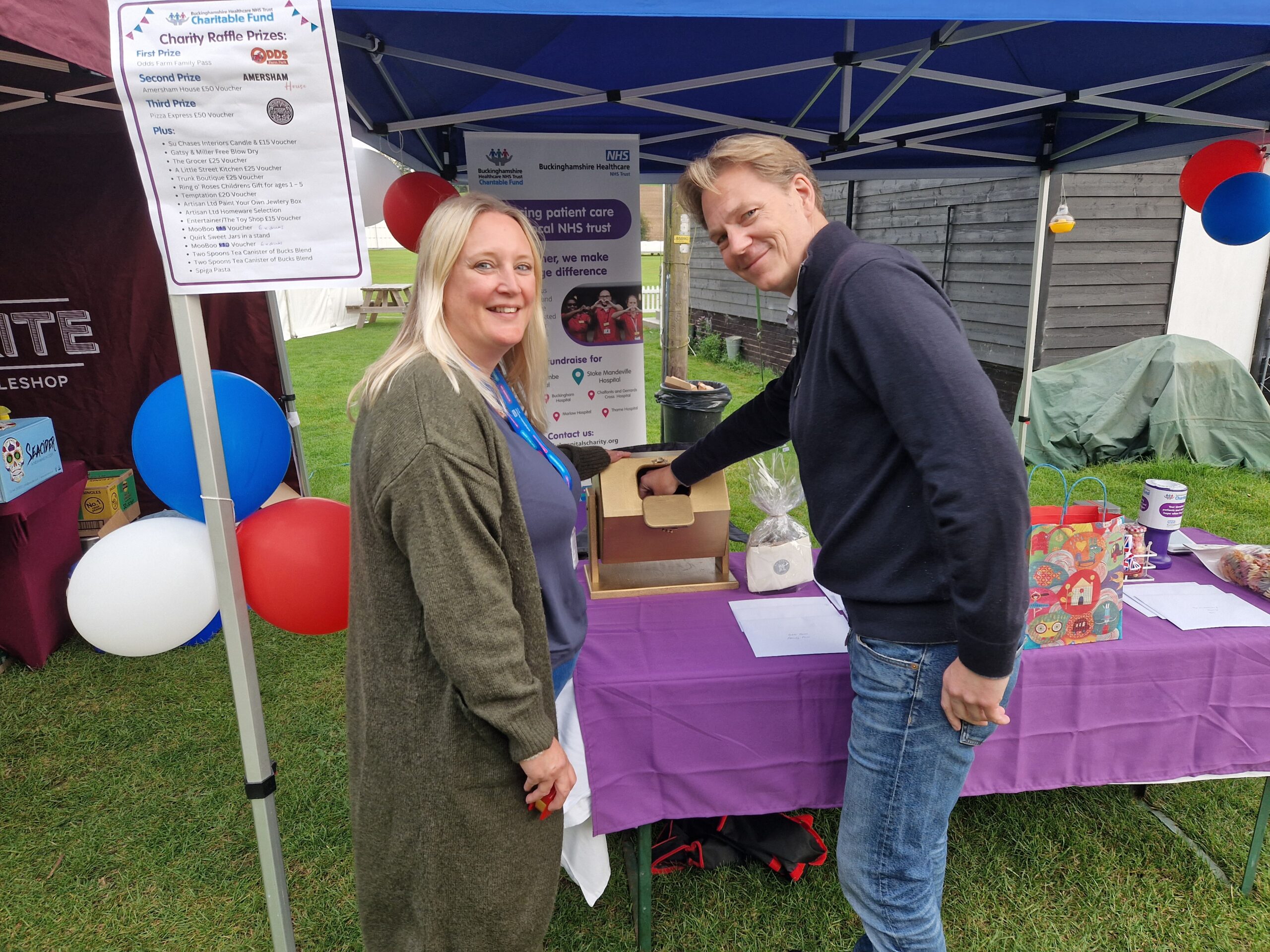 Sophie from the Charity and Mark from Amersham Community Board drawing a raffle ticket whilst looking towards the camera.