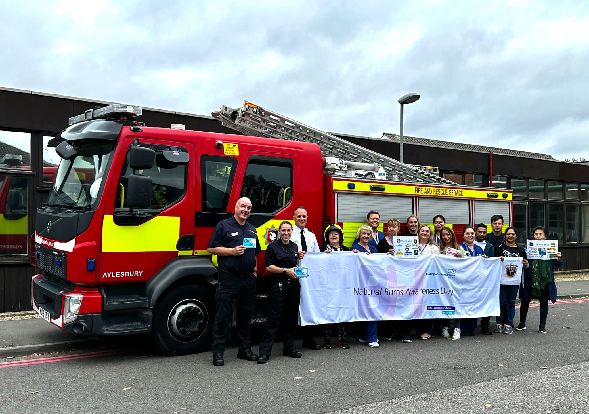 The Burns team holding a National Burns Awareness Day banner in front of a fire truck with some fire fighters.