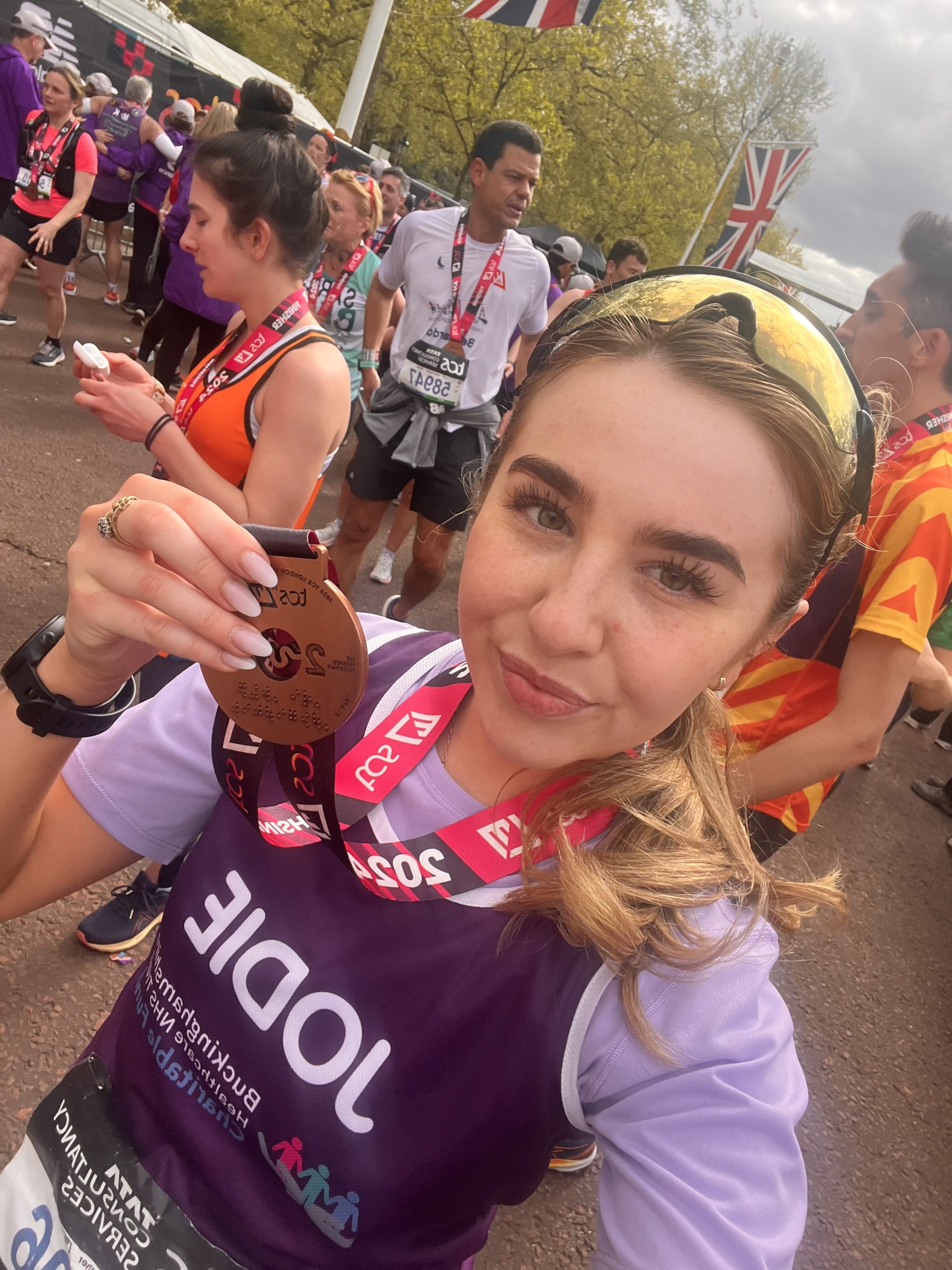 Jodie Holding her London Marathon Medal wearing a purple Buckinghamshire Healthcare NHS Trust Charitable Fund running vest