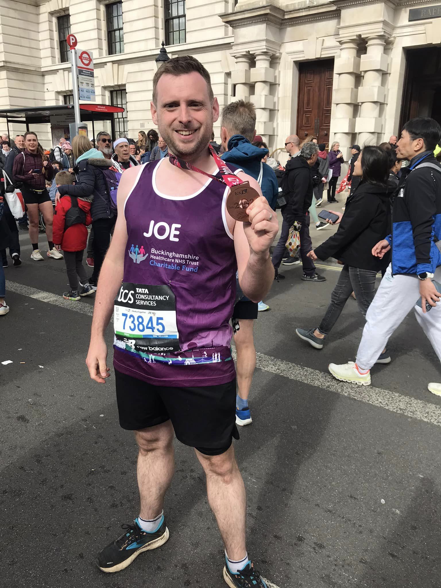 Joe Holding his London Marathon Medal wearing a purple Buckinghamshire Healthcare NHS Trust Charitable Fund running vest